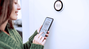 Personne réglant un thermostat intelligent mural à l'aide d'un smartphone.