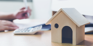 Modèle en bois d'une maison sur un bureau avec une calculatrice et une personne en train d'écrire.