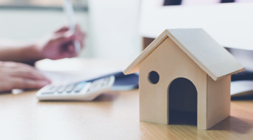 Modèle en bois d'une maison sur un bureau avec une calculatrice et une personne en train d'écrire.