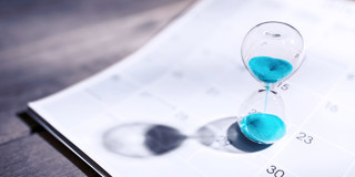 Zandloper met blauwe zandkorrels op een kalender, symbool voor de passage van tijd en planning.