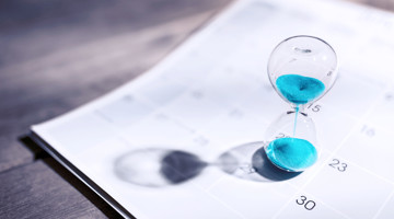 Zandloper met blauwe zandkorrels op een kalender, symbool voor de passage van tijd en planning.