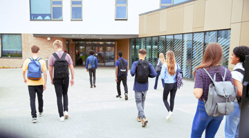 Des étudiants marchent vers l'entrée d'un bâtiment scolaire.
