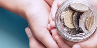 Deux mains tiennent un bocal en verre rempli de pièces de monnaie.