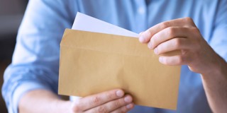 Une personne portant une chemise bleu clair ouvre une enveloppe brune et en retire une lettre blanche.