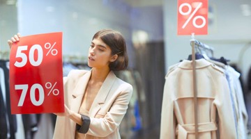 Een persoon houdt verkoopborden vast met '50%' en '70%' in een kledingwinkel.
